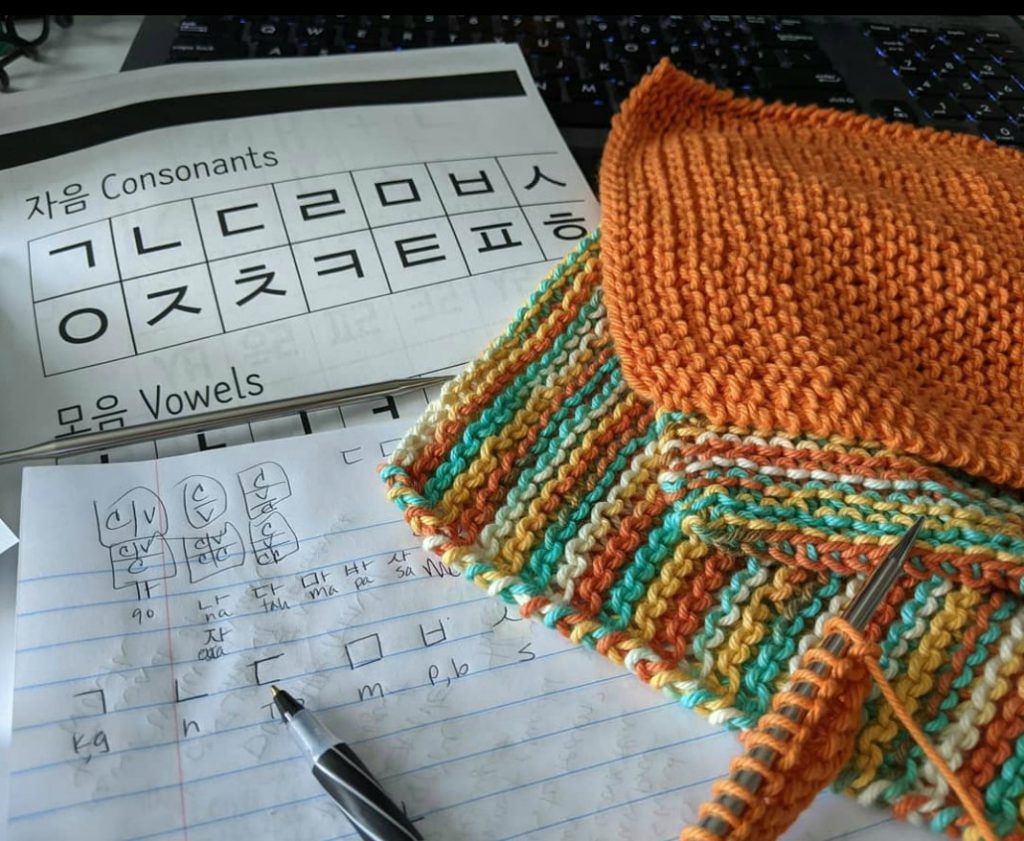 Bright hand knitted washcloths sitting next to a notebook and paper handouts with Korean letters printed on them.